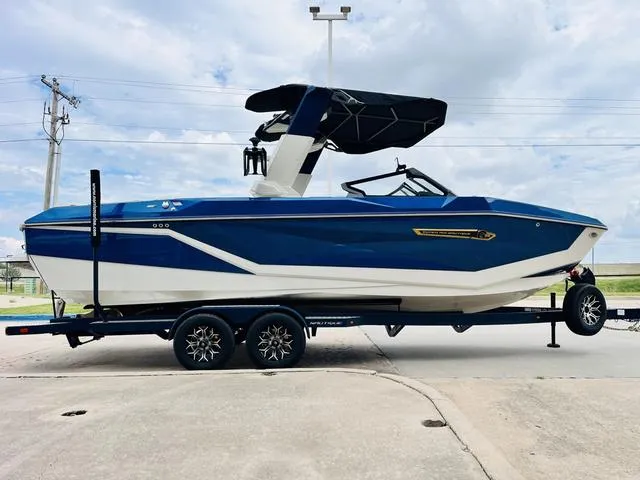 Slide: The Image of 2025 Nautique SUPER AIR G G25 boat on trailer, blue and white design, parked outdoors. - 5