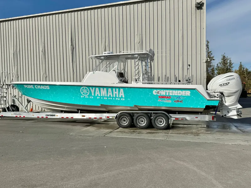 Slide: The Image of 2024 Contender 39 Fisharound boat on trailer, Yamaha engines, turquoise hull, parked by a building. - 9