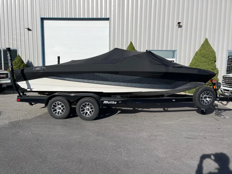 Slide: The Image of 2024 Nautique Ski Nautique boat covered on a trailer, parked outside a building. - 21