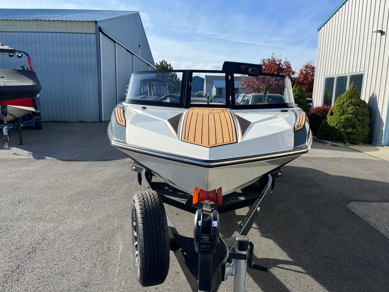 Slide: The Image of 2024 Nautique Ski Nautique boat on trailer, parked outdoors near metal buildings. - 23