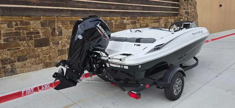 Slide: The Image of 2025 Tahoe T16 boat on trailer with Mercury outboard motor, parked by stone wall. - 4