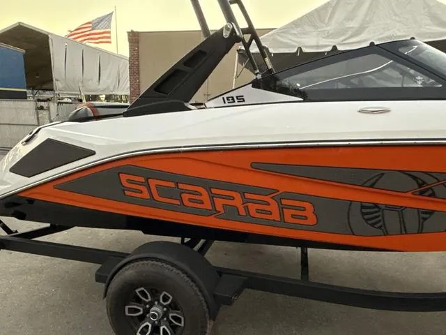 Slide: The Image of 2025 Scarab 195 LX boat with orange and black design on a trailer. - 14