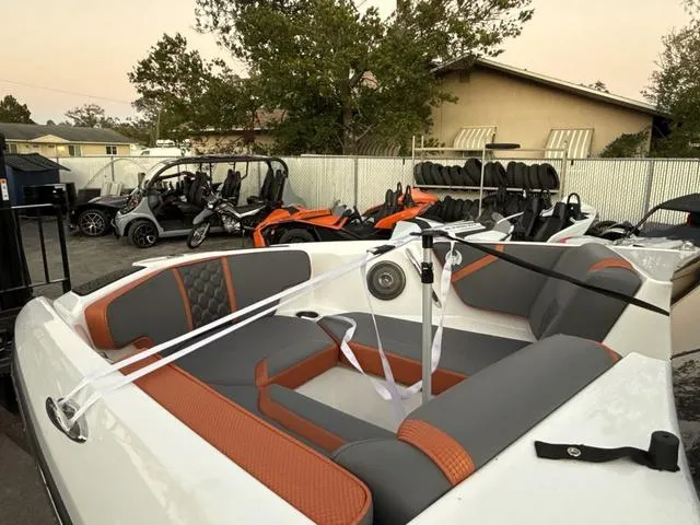 Slide: The Image of 2025 Scarab 195 LX boat with orange and gray seating, parked near golf carts and ATVs. - 5