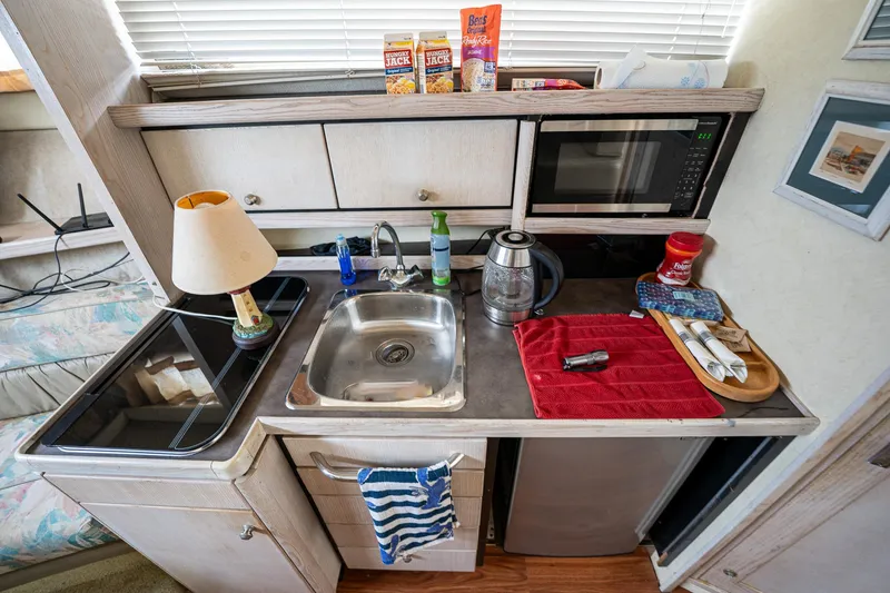 Slide: The Image of Compact kitchen area in a 1997 Bayliner 3255 Avanti boat, featuring a sink, microwave, and stove. - 30
