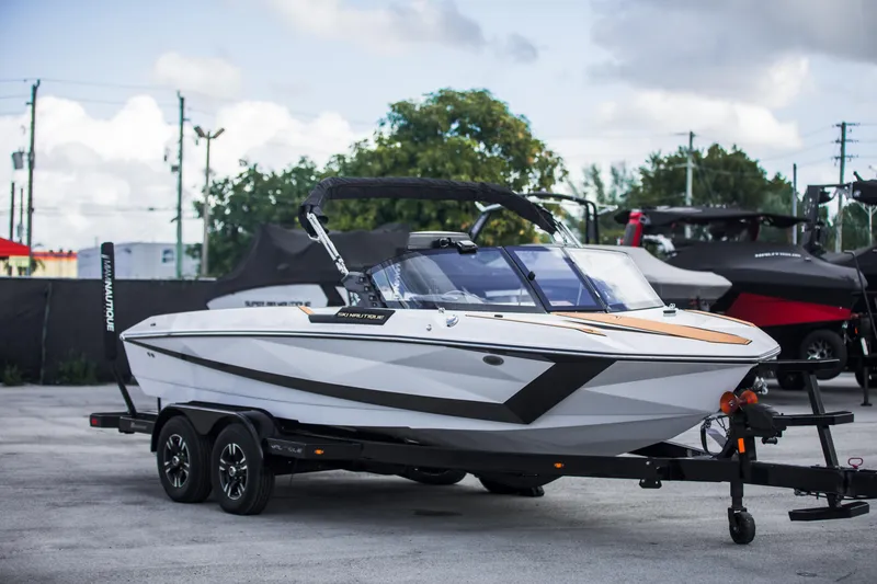The Image of 2025 Nautique Ski boat on trailer, sleek design, parked outdoors. - 0