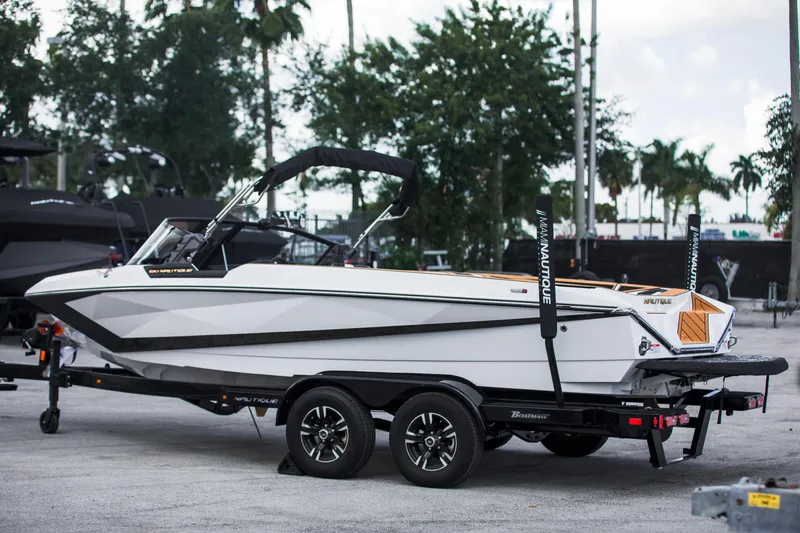 Slide: The Image of 2025 Nautique Ski boat on trailer, parked outdoors with trees in background. - 7