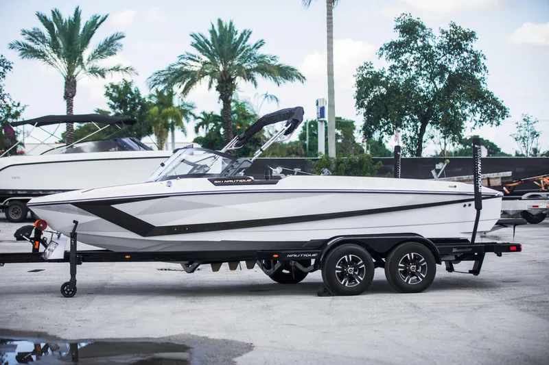Slide: The Image of 2025 Nautique Ski boat on trailer, parked outdoors with palm trees in background. - 8