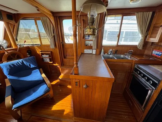 Slide: The Image of 1983 DeFever 41 Trawler interior with wooden cabinetry, blue chair, and kitchen area. - 21