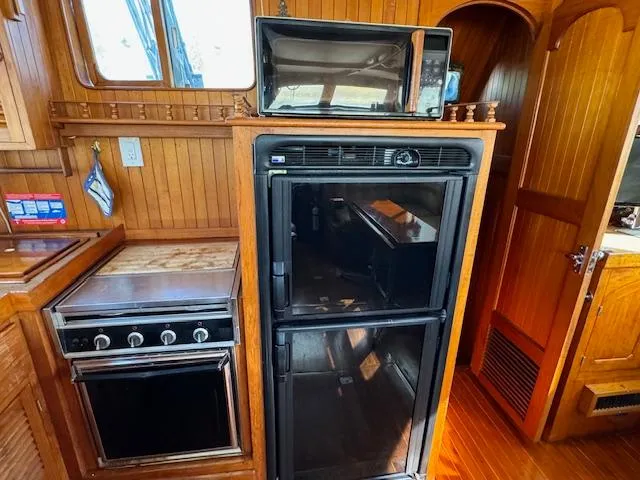 Slide: The Image of 1983 DeFever 41 Trawler kitchen with stove, fridge, and microwave in wooden interior. - 23