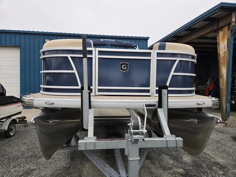 Slide: The Image of 2025 Godfrey Sweetwater 2086 C pontoon boat on trailer, parked near blue building. - 7