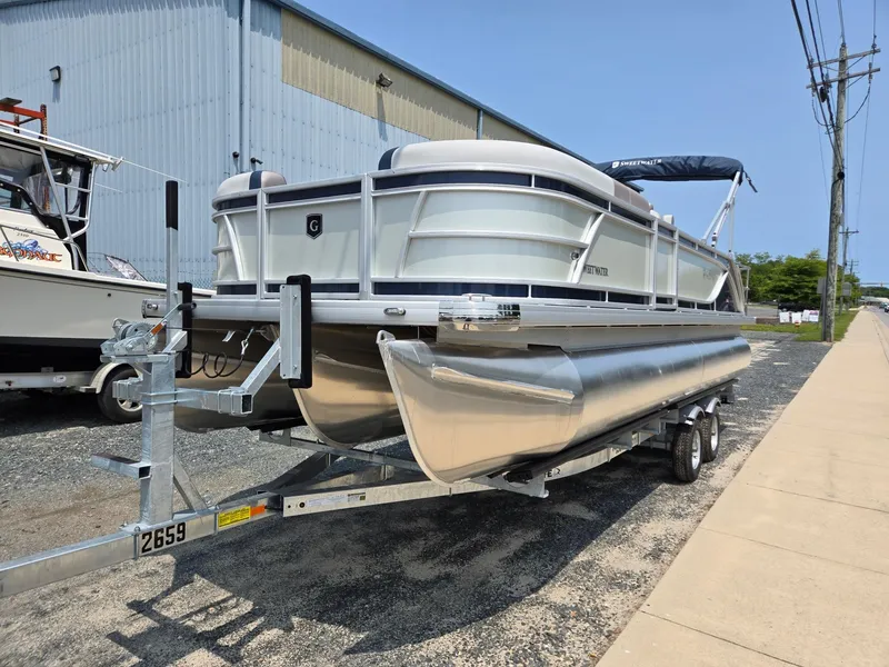 Slide: The Image of 2025 Godfrey SWEETWATER 2286 SFL pontoon boat on trailer, parked near industrial building. - 0