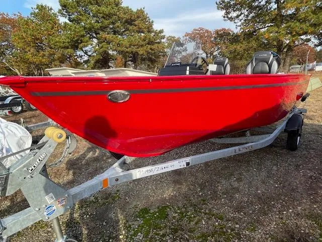 The Image of 2025 Lund 1650 Angler SS boat in vibrant red on a trailer, surrounded by trees. - 0