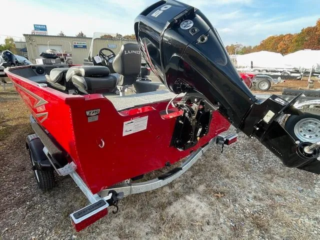 Slide: The Image of 2025 Lund 1650 Angler SS boat with outboard motor, red exterior, parked outdoors. - 2