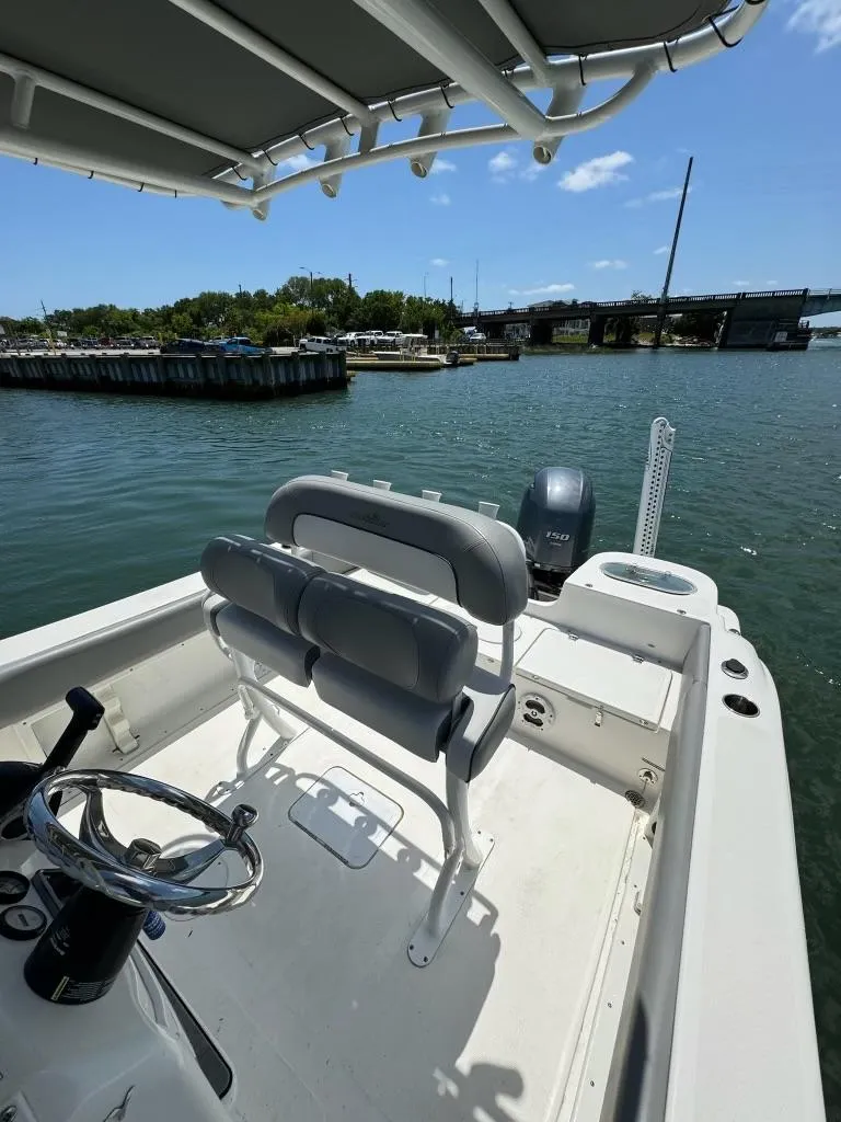 Slide: The Image of 2022 NauticStar 2102 Legacy boat interior with helm and seating, docked by a scenic waterfront. - 11