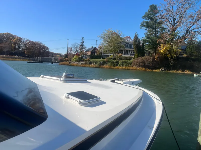 Slide: The Image of 1993 Bertram 37 Convertible boat docked on a serene river with houses in the background. - 5