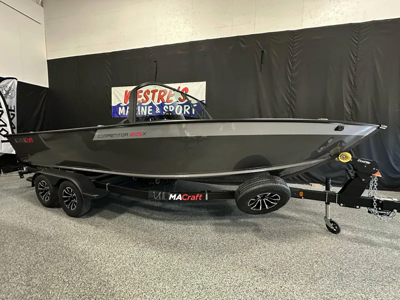 The Image of 2025 Alumacraft Competitor 205X Sport boat on trailer in showroom setting. - 0