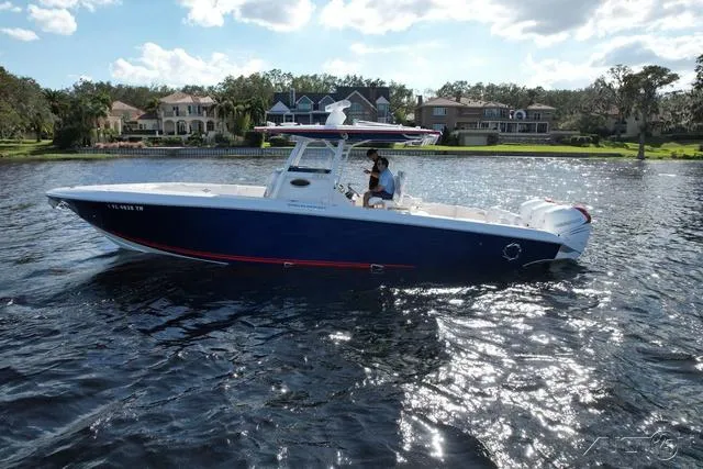 The Image of 2023 Fountain 34 CC boat cruising on a sunny lake near waterfront homes. - 1