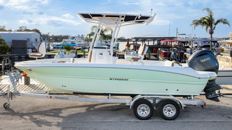 Slide: The Image of 2025 Stingray 216CC boat on trailer, dockside with Yamaha engine, sunny day. - 1