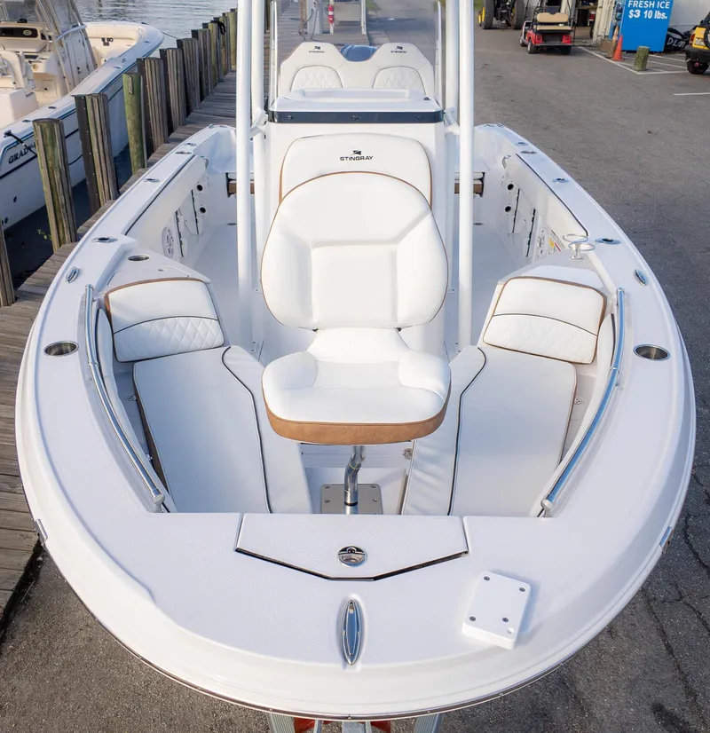 Slide: The Image of 2025 Stingray 216CC boat with white seating and sleek design at a marina. - 2