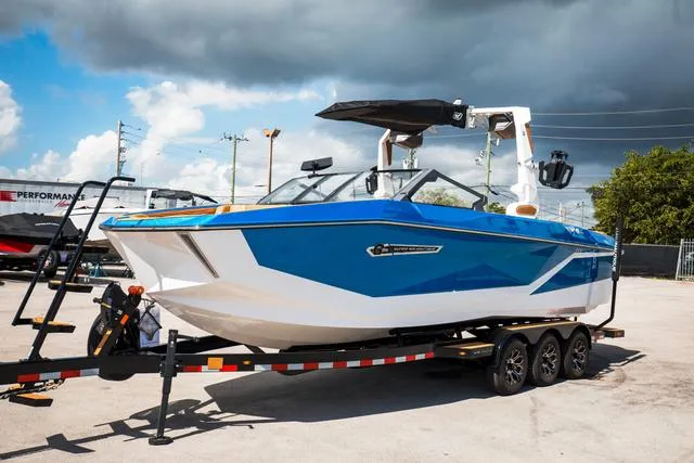 Slide: The Image of 2025 Nautique G25 boat on trailer, blue and white design, parked outdoors. - 10