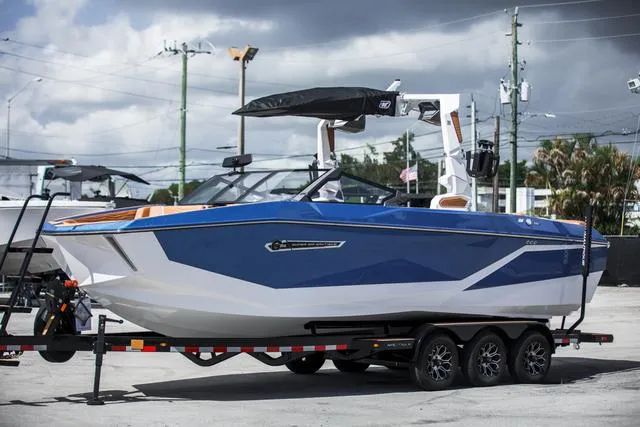 Slide: The Image of 2025 Nautique G25 boat on trailer, blue and white design, parked outdoors. - 2