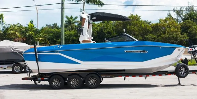 Slide: The Image of 2025 Nautique G25 boat in blue and white on a trailer, parked outdoors. - 7
