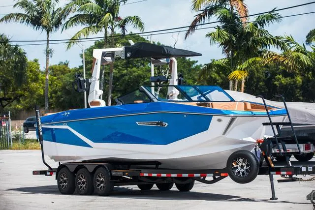 Slide: The Image of 2025 Nautique G25 boat on trailer, blue and white design, parked near palm trees. - 8