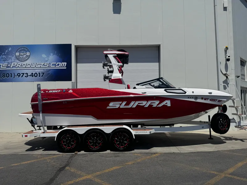 The Image of 2023 Supra SL 550 boat on trailer, red and white design, parked outside a building. - 0
