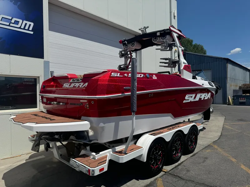 Slide: The Image of 2023 Supra SL 550 boat in red, parked on a trailer outside a building. - 2