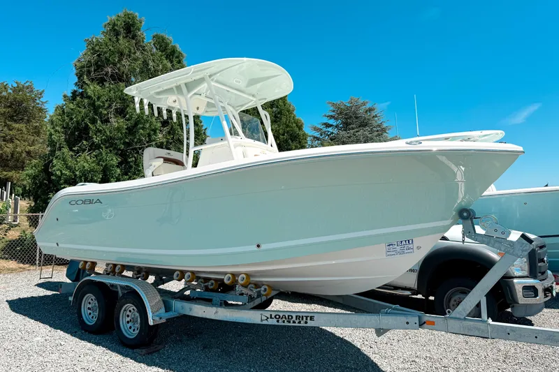 The Image of 2025 Cobia 220 Center Console boat on trailer, parked outdoors under clear blue sky. - 0