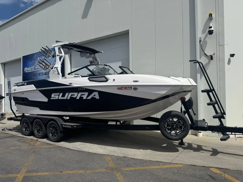 Slide: The Image of 2023 Supra SE 550 boat on trailer, parked outside a building. - 2