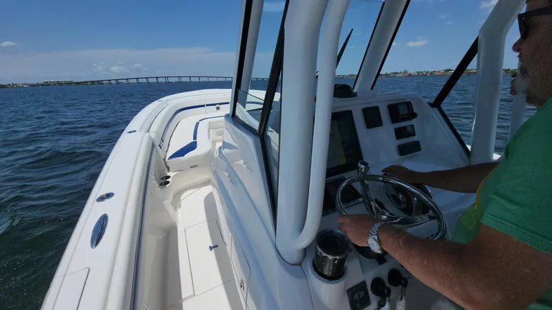 Slide: The Image of 2015 Intrepid 327 Center Console boat on water, person steering, clear sky, distant bridge. - 35