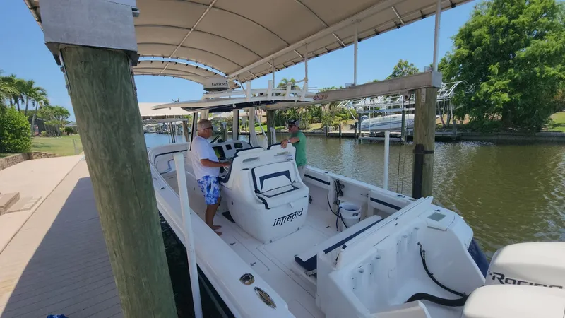 Slide: The Image of 2015 Intrepid 327 Center Console boat docked under canopy, with two people on board. - 40