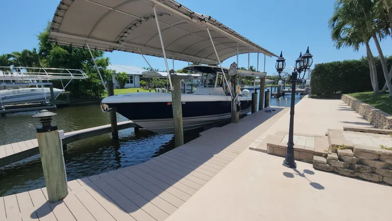 Slide: The Image of 2015 Intrepid 327 Center Console boat docked under a canopy in a sunny marina. - 44