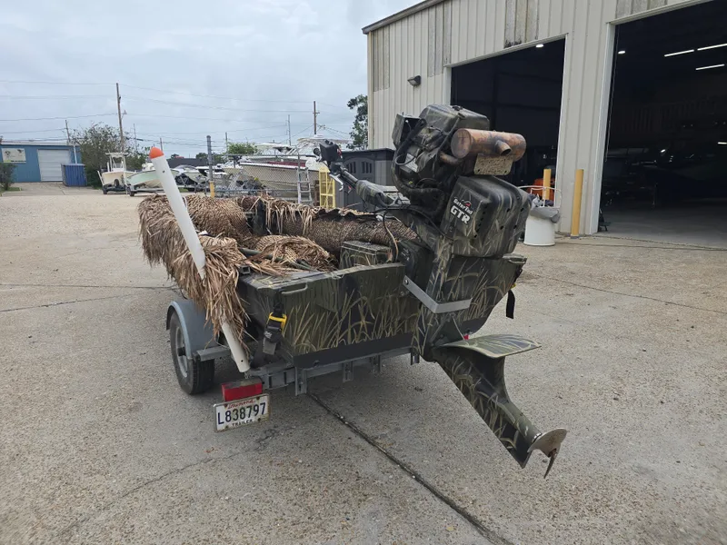 Slide: The Image of Custom Shallow 16 boat, 2016 model, with camouflage design and outboard motor, parked outside a garage. - 4
