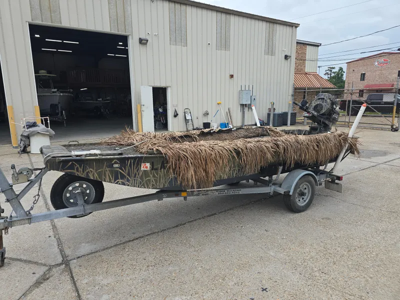 Slide: The Image of Custom Shallow 16 boat, 2016 model, camouflaged with grass, on a trailer outside a workshop. - 5