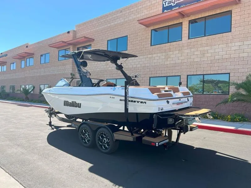 Slide: The Image of 2025 Malibu 23 LSV boat on trailer, parked near brick building. - 3