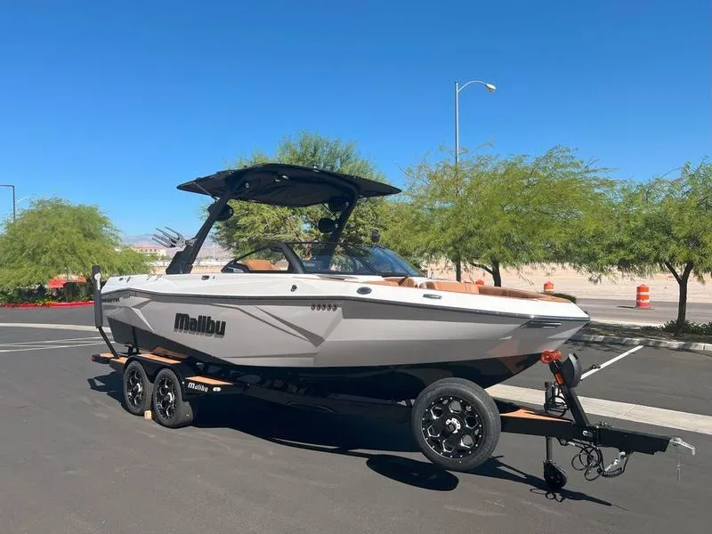 Slide: The Image of 2025 Malibu 23 LSV boat on trailer, parked outdoors under clear blue sky. - 4