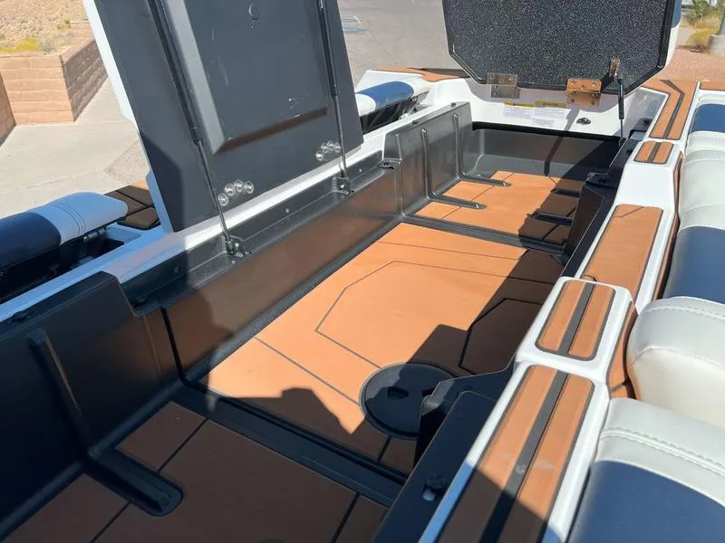 Slide: The Image of 2025 Malibu 25 LSV boat interior with open storage compartments and cushioned seating. - 16