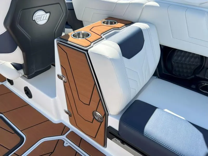 Slide: The Image of 2025 Malibu 25 LSV boat interior with white and blue seating, wood accents, and cup holders. - 9