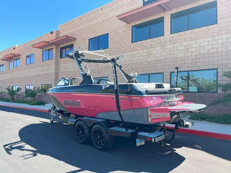 Slide: The Image of 2021 Malibu 22 LSV boat in vibrant pink, parked outside a modern building. - 2