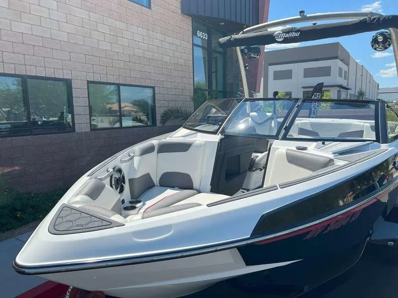 Slide: The Image of 2021 Malibu 22 LSV boat with sleek design, parked near modern building. - 6