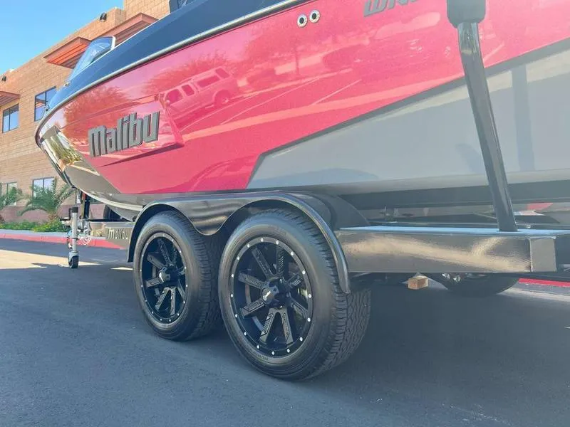 Slide: The Image of 2021 Malibu 22 LSV boat on trailer with black wheels, parked outdoors. - 7