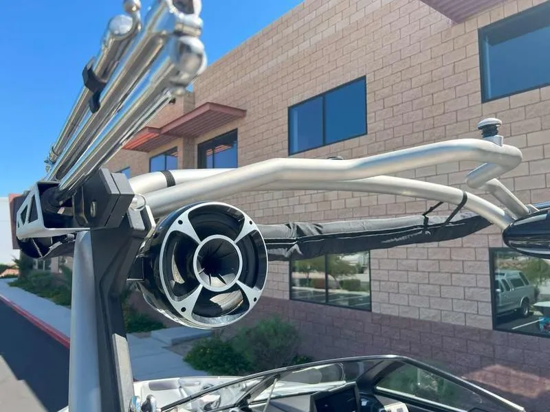 Slide: The Image of 2021 Malibu 22 LSV boat with wakeboard tower and speaker, parked near a brick building. - 9