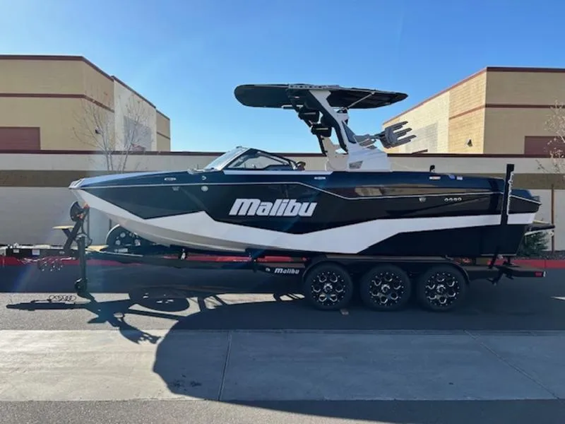 Slide: The Image of 2025 Malibu M242 boat on trailer, sleek black and white design, parked outdoors. - 1