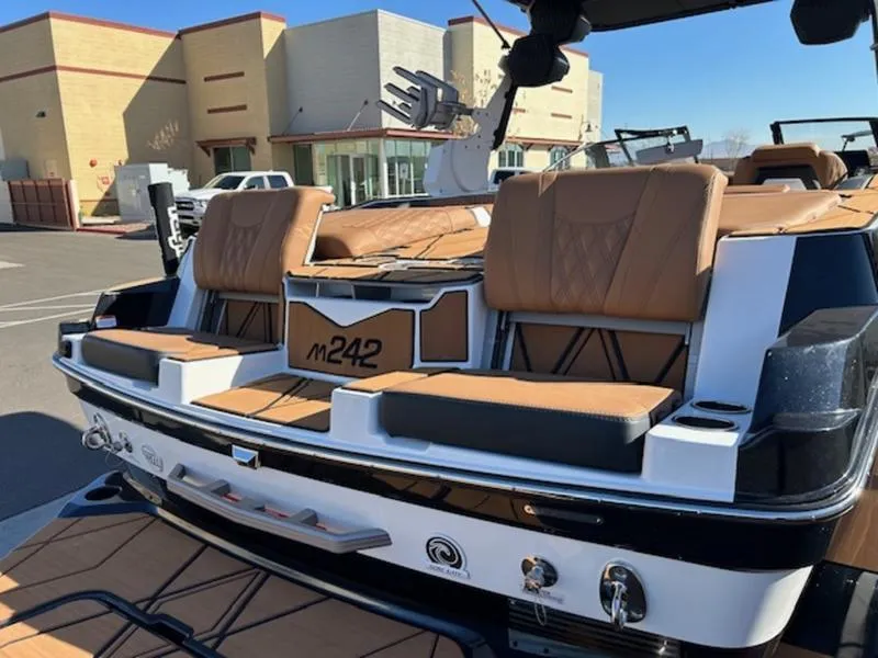 Slide: The Image of 2025 Malibu M242 boat with tan seating and sleek design in a parking lot. - 32