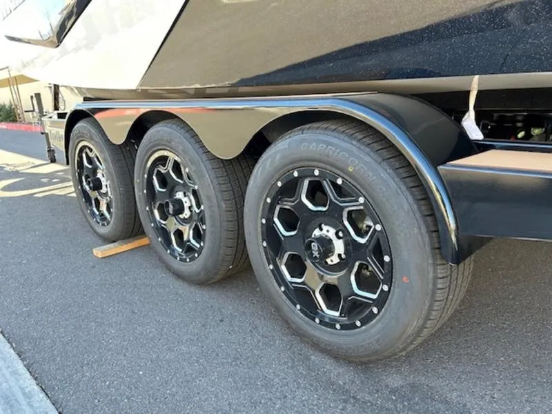 Slide: The Image of 2025 Malibu M242 boat trailer with triple black wheels on asphalt. - 7