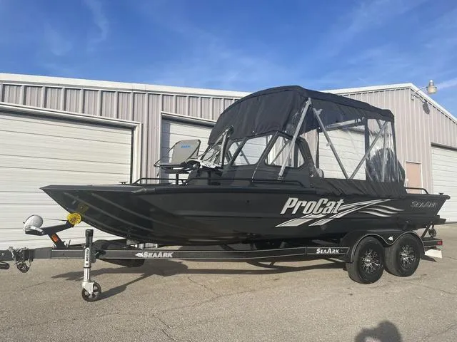 Slide: The Image of 2025 SeaArk Pro Cat 200 boat with canopy on trailer, parked near garages. - 2