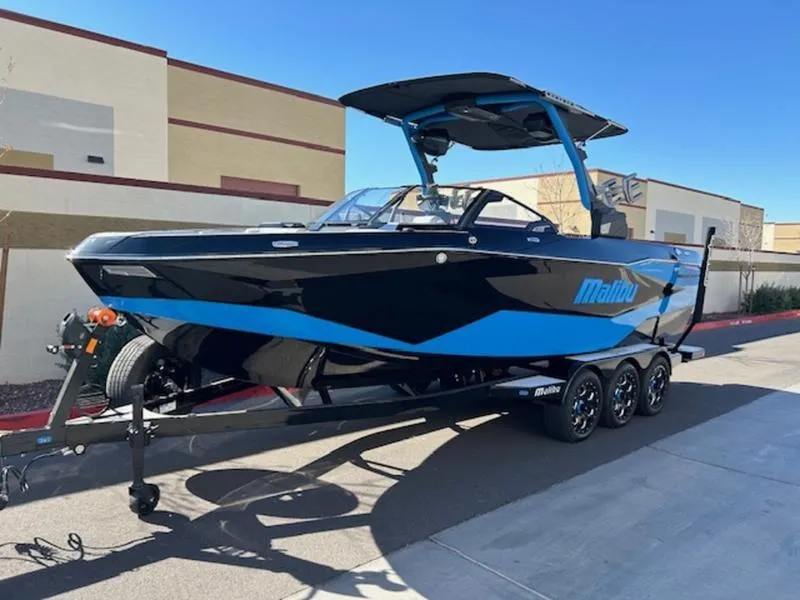 Slide: The Image of 2025 Malibu 25 LSV boat on trailer, black and blue design, parked outdoors. - 3