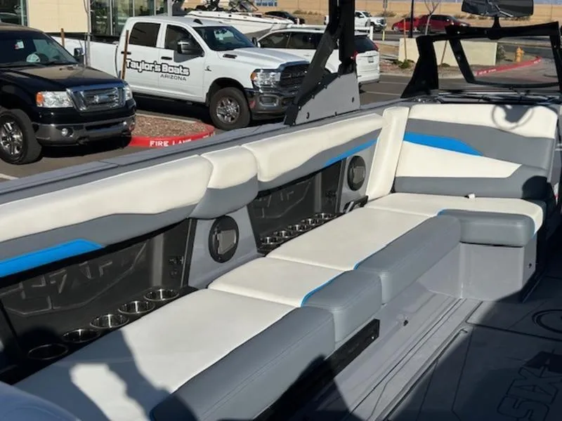 Slide: The Image of 2024 Axis T250 boat interior with white and blue seating, cup holders, and parked vehicles nearby. - 9